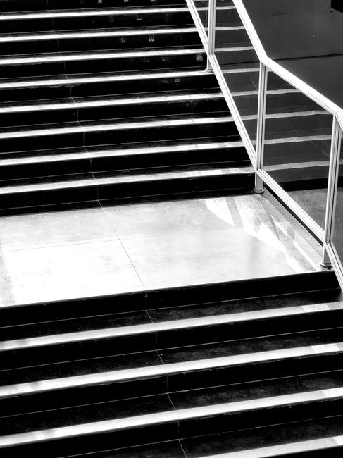 A close-up view of a modern staircase with black polished stone steps featuring white strip lighting along the edges, adjacent to a glass and stainless steel railing. The surrounding floor area is mad