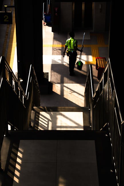 Exterior view of Hammersmith station in London, featuring railway tracks running through an underground area with a covered walkway on the side. The station has a modern design with white tiled walls,